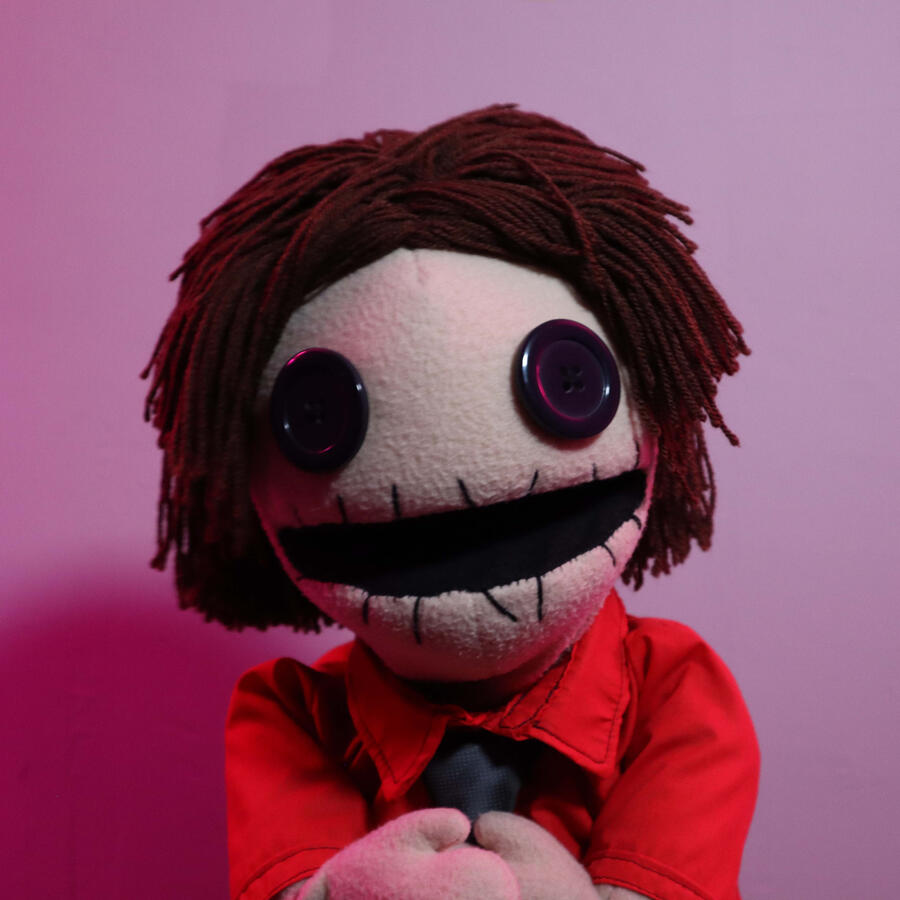 A hand-operated puppet made from scratch using sponge foam, various fabrics and a knitting-wool wig. Includes a button-up shirt, a t-shirt made to fit a small character and swappable arms for performance with live-hands & arm-rods.