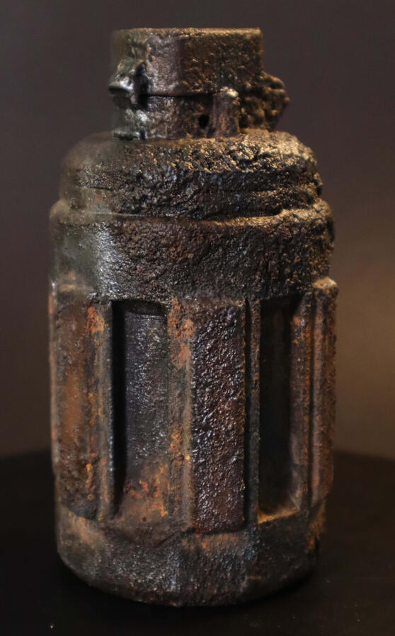 Grenade prop textured and painted to look as if it has been dug up, with caked dirt and signs of rust.